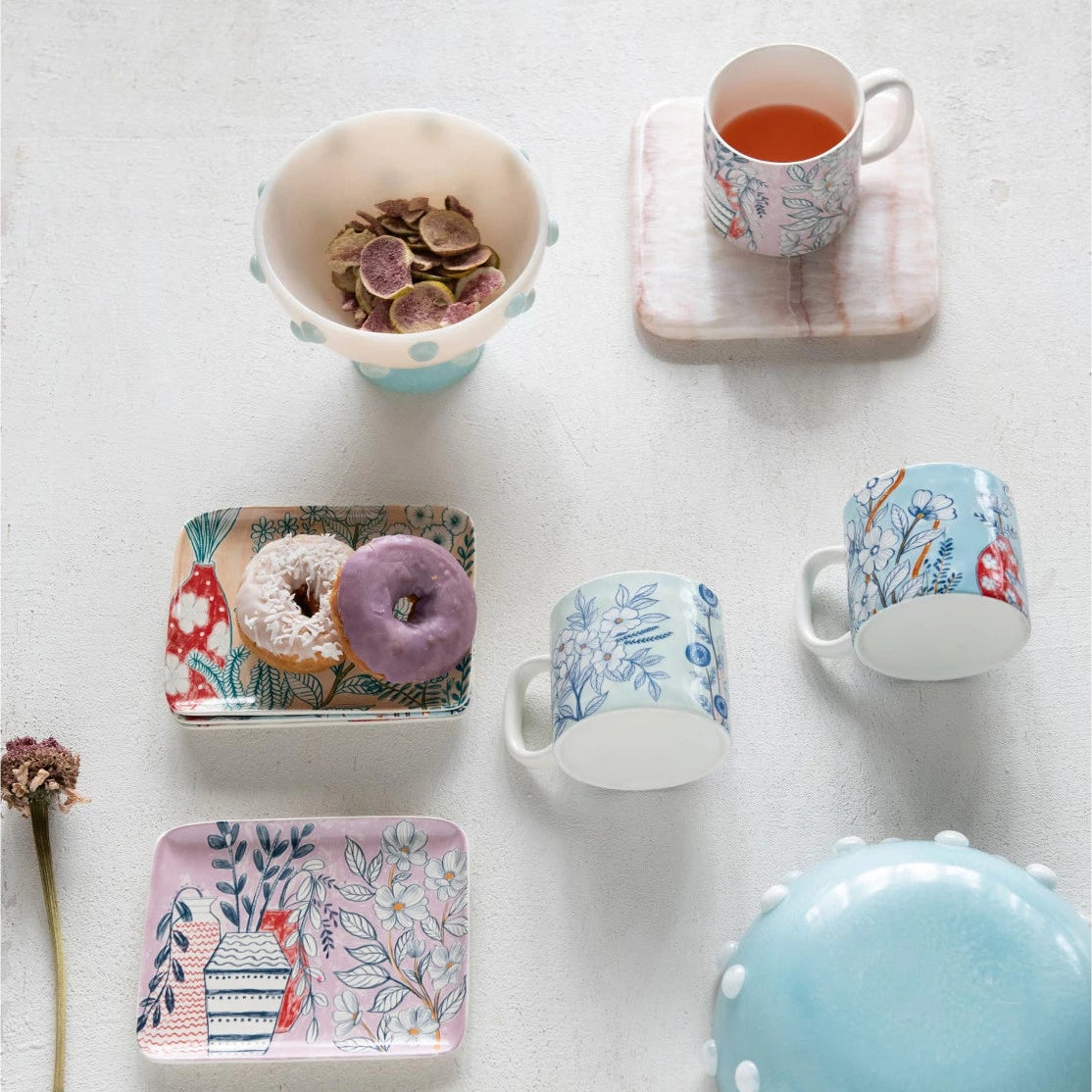 Collection of ceramic items including mugs, bowls, and a small tray with floral designs on a white surface.
