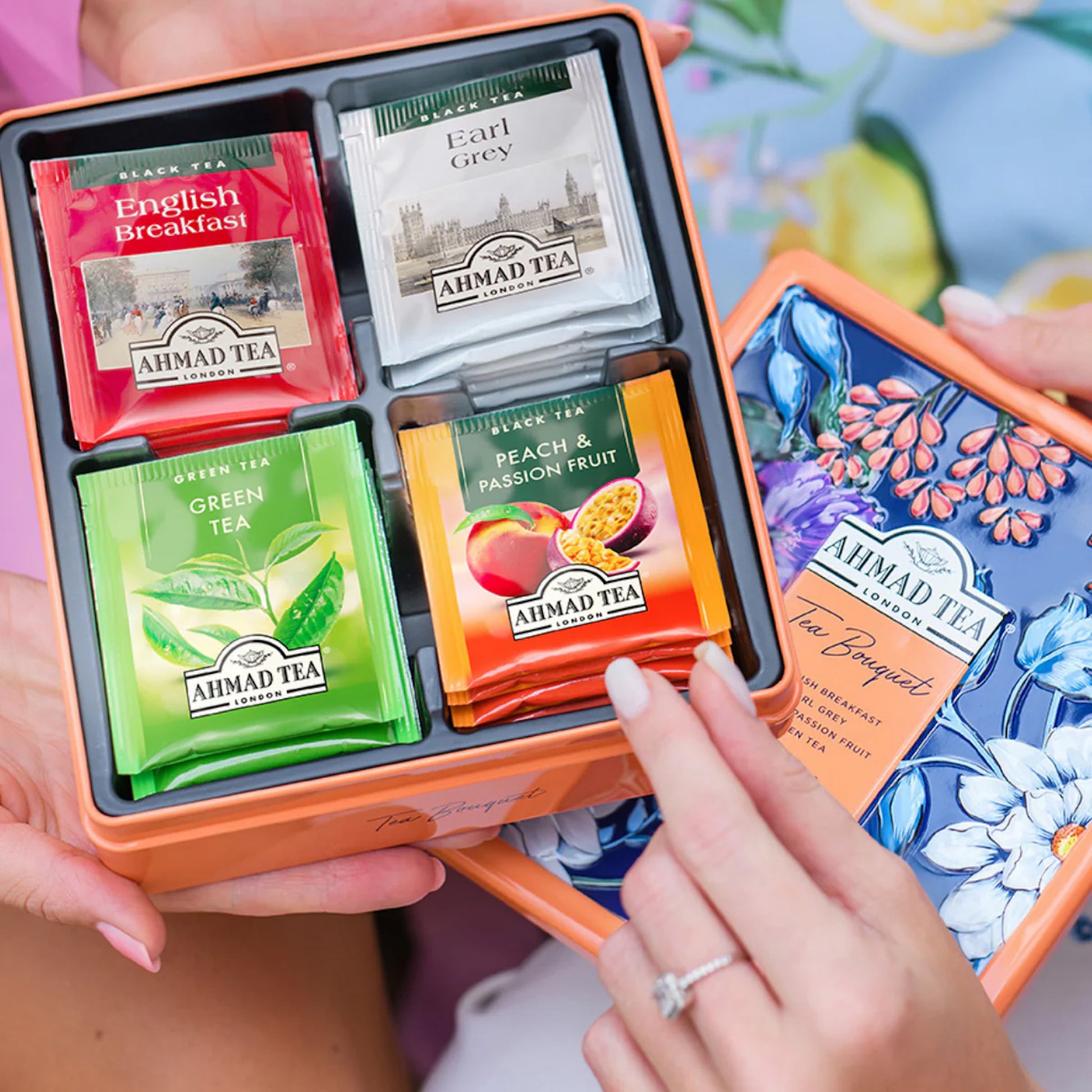 hands holding open tin of Ahmad teas showing assortment in side