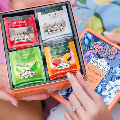 hands holding open tin of Ahmad teas showing assortment in side