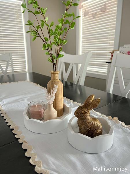 Two sizes of round white trays set in the center of a table with decorative items in them.