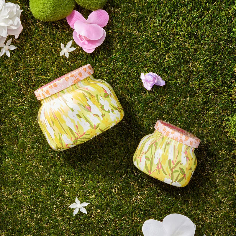 2 sizes of aolha orchid candles set on a grassy surface with flowers scattered about.