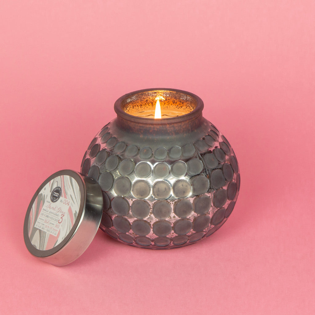 lit candle in grey glass container on a pink background.