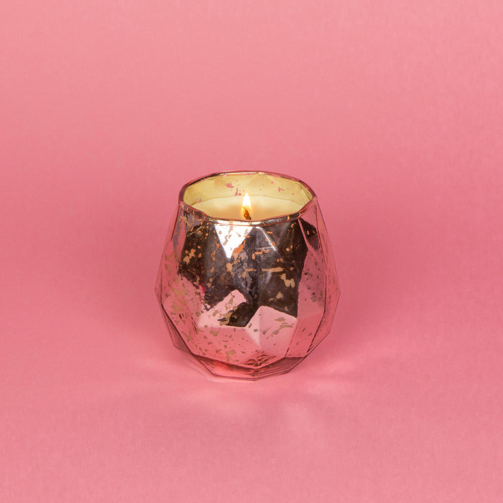 lit candle in a pink mercury glass container on a pink background.
