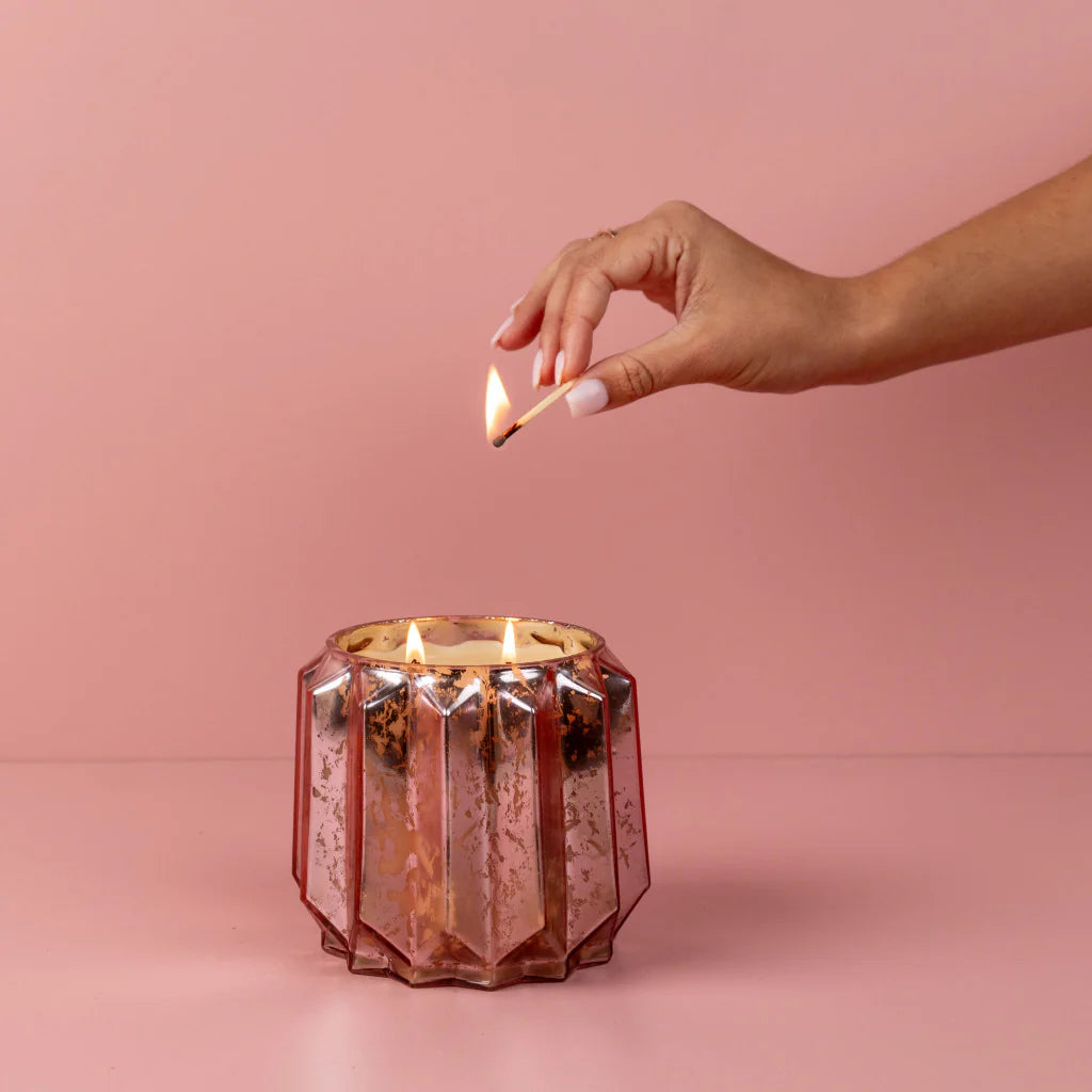 Hand lighting a candle in a decorative pink holder against a pink background