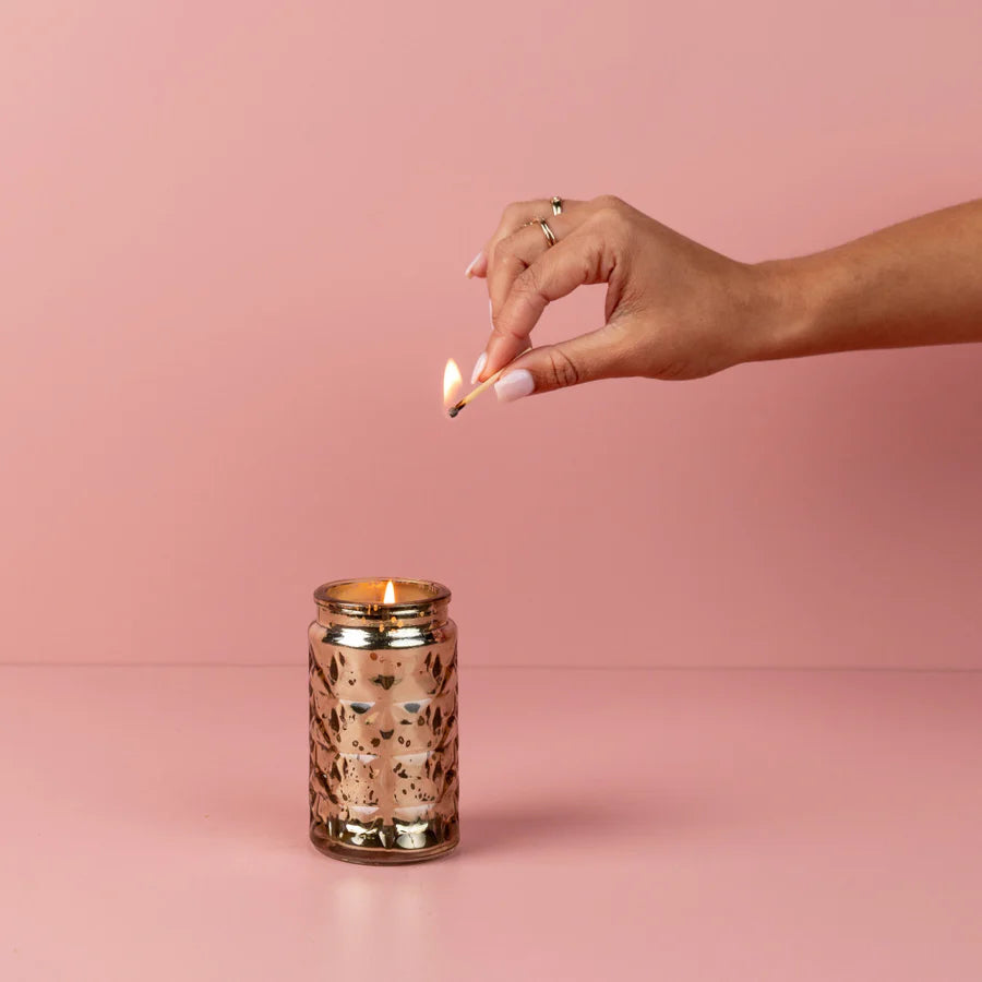 Hand lighting a candle with a pink background