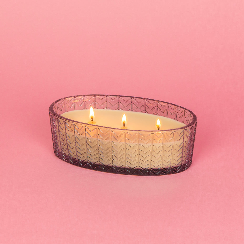 lit candle on oval glass bowl on a pink background.