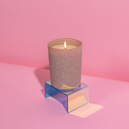 lit candle in pink speckled container on a pink background.