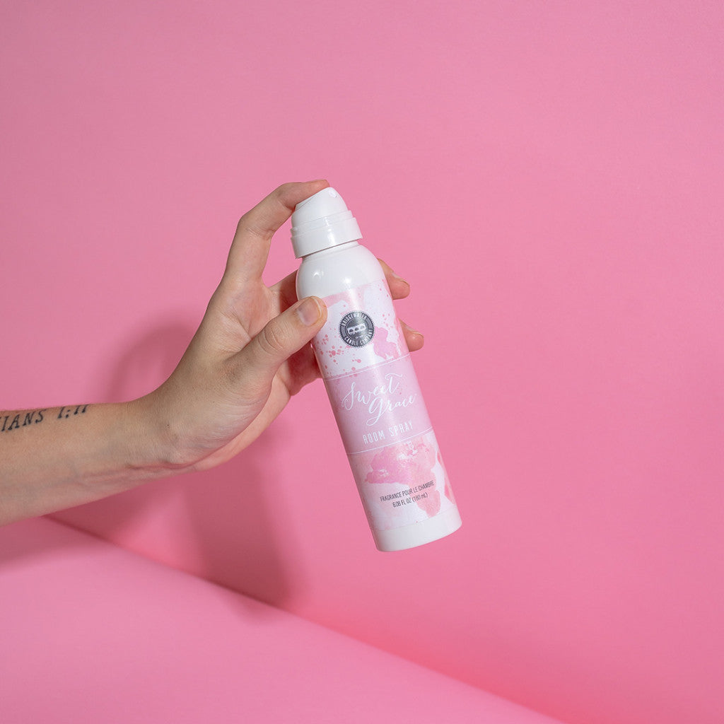 hand holding bottle of room spray against a pink background.