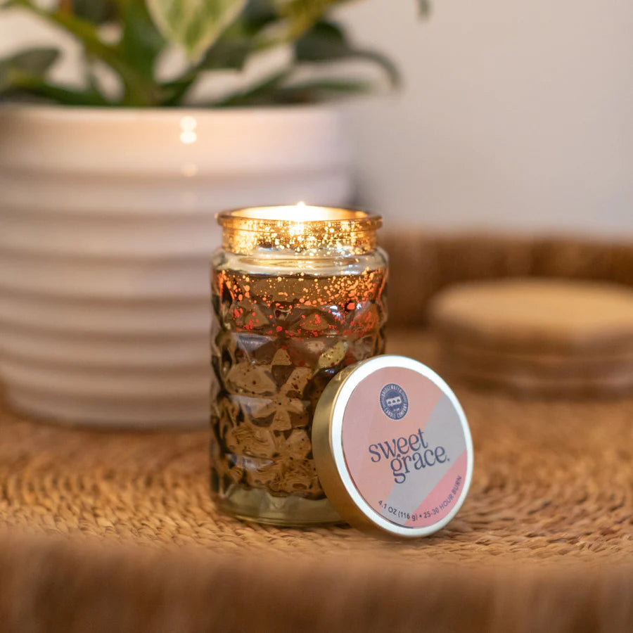 Candle in a decorative jar with 'sweet grace' lid on a woven surface.