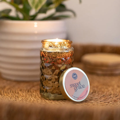Candle in a decorative jar with 'sweet grace' lid on a woven surface.