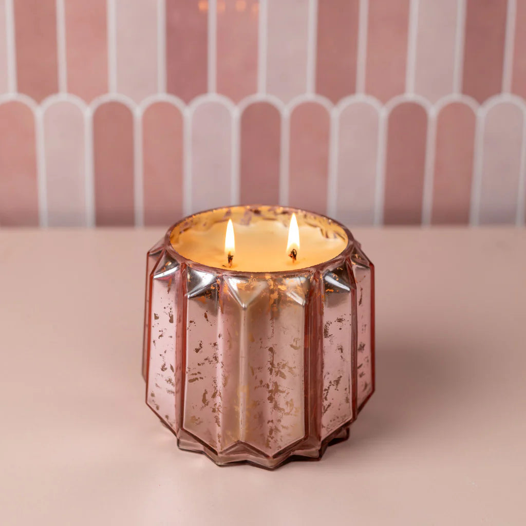 Pink glass candle holder with a lit candle on a pink background