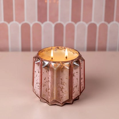 Pink glass candle holder with a lit candle on a pink background