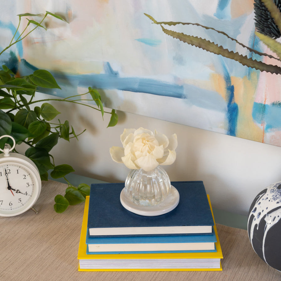 Bella Freesia Flower Diffuser set on a stack of books on a table with a  plant and a clock.