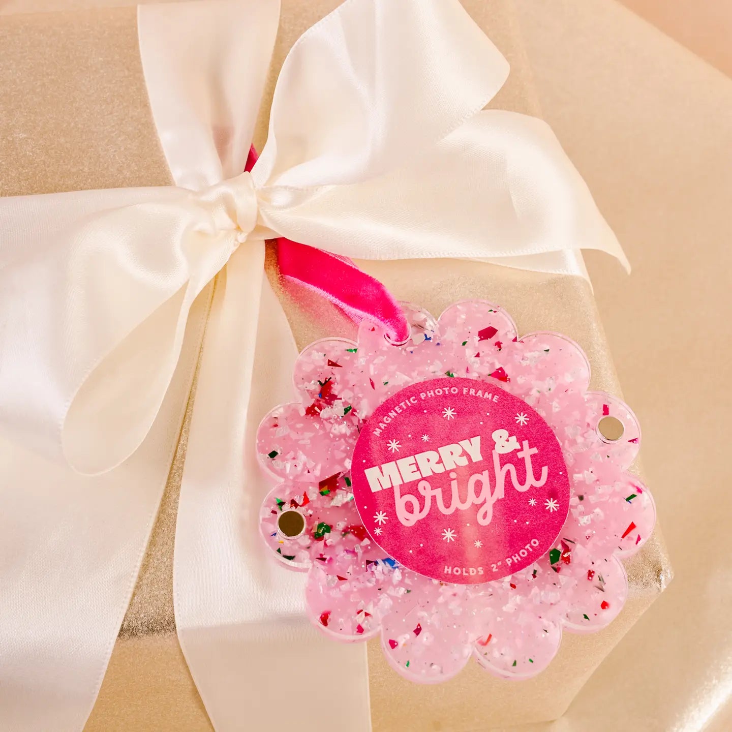 Pink Confetti round ornament frame tied in an ivory bow on a wrapped gift
