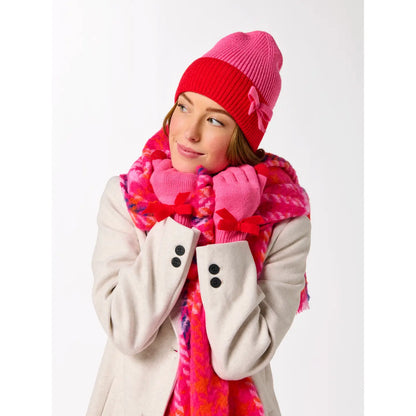 person wearing white coat, pink and red scarf and pink and red beanie with bow on cuff