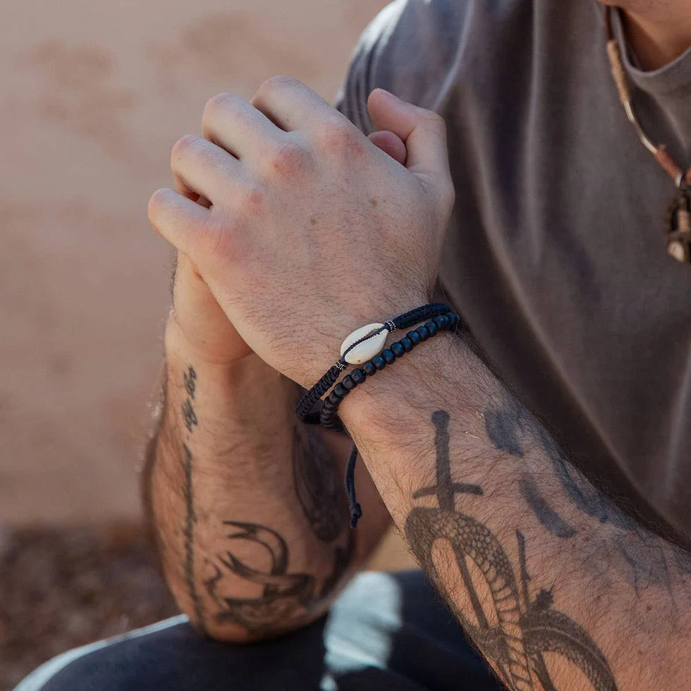 Person with tattoos wearing a bracelet on a blurred natural background