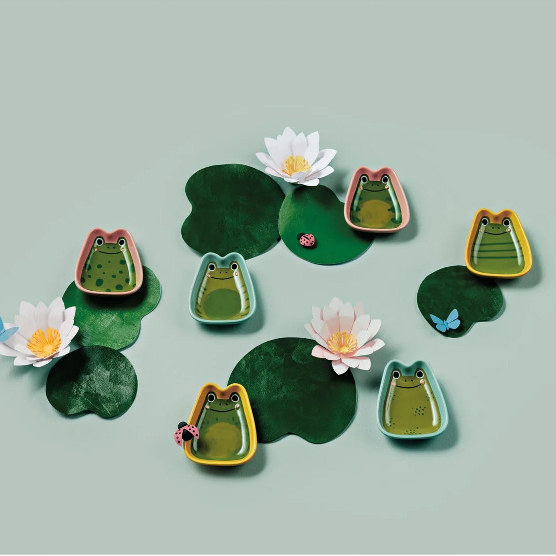 Frog dishes  and water lilies on green leaves against a light gray background