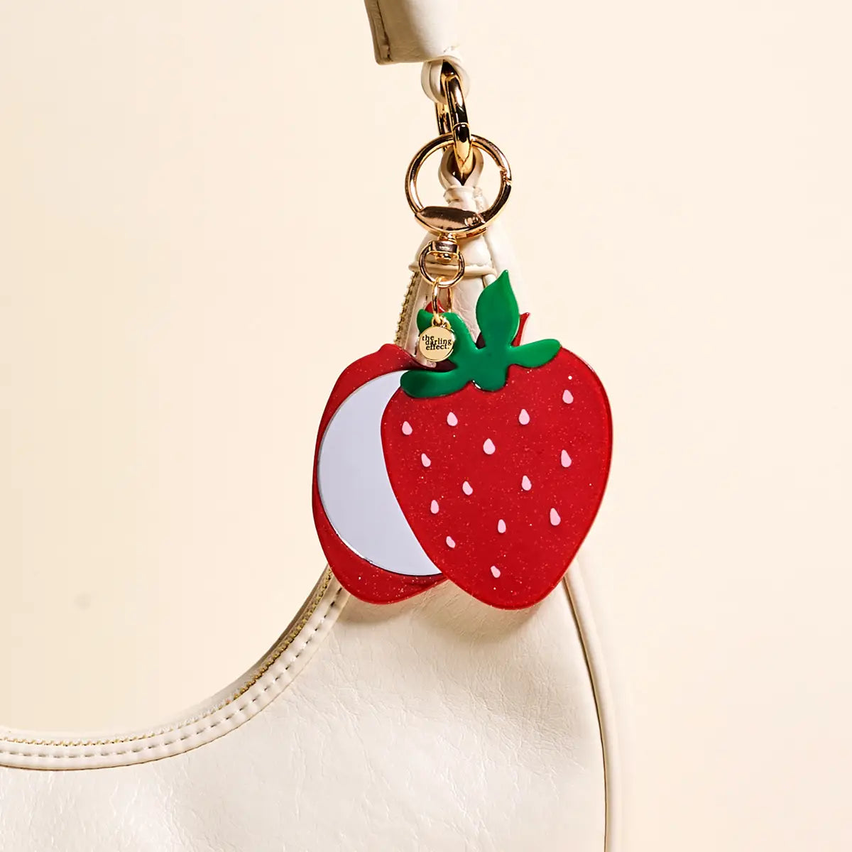 Strawberry-shaped keychain attached to a beige bag
