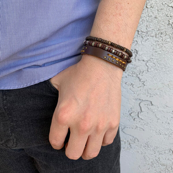 2 wood bead stretch bracelets and one leather band bracelet on a person's wrist.