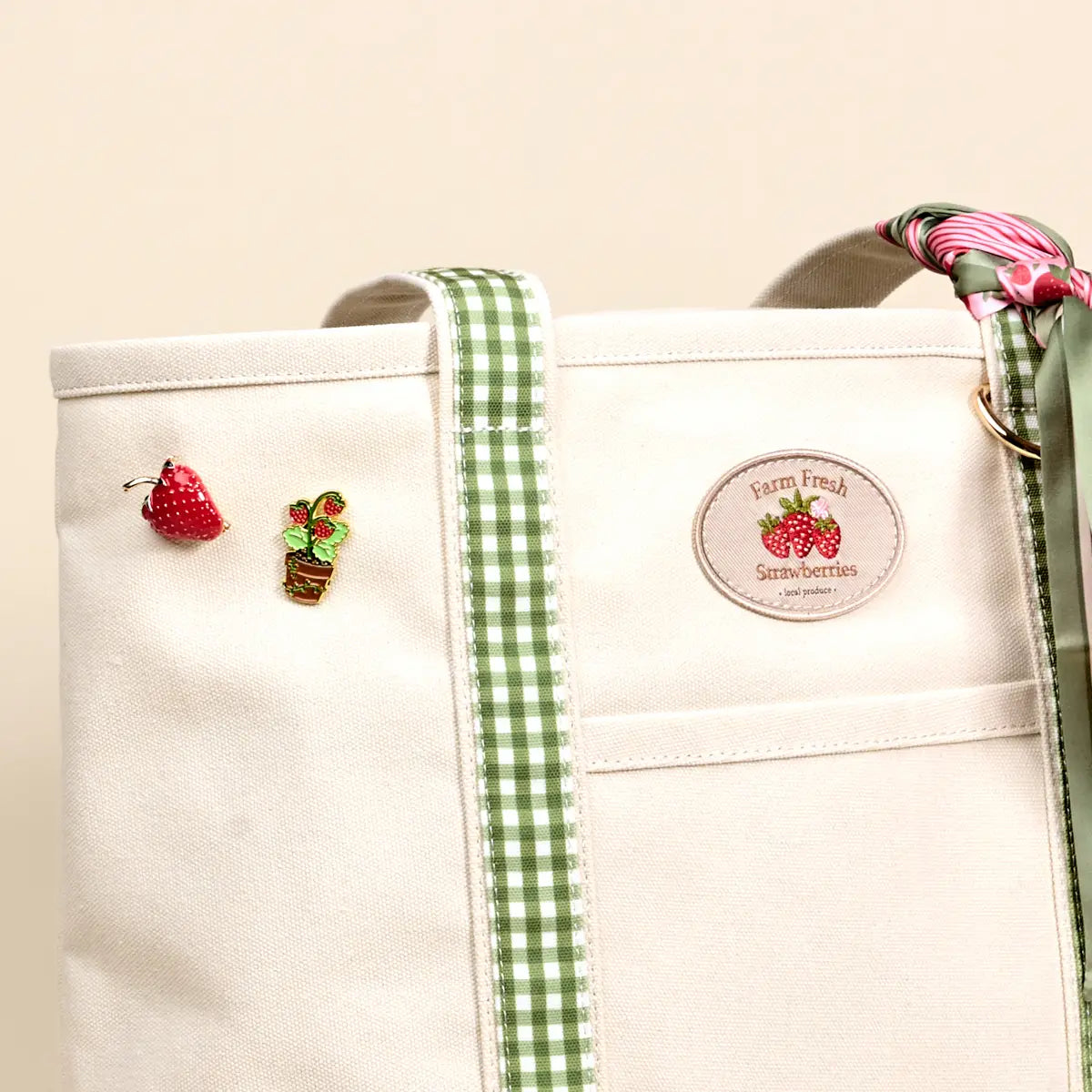 close-up of Off-White tote bag with green gingham strap, strawberry-themed decorations, and a label on a beige background.
