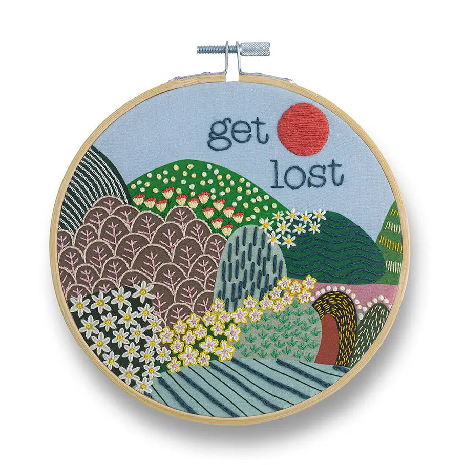 Embroidery hoop with colorful landscape design and 'get lost' text on a white background