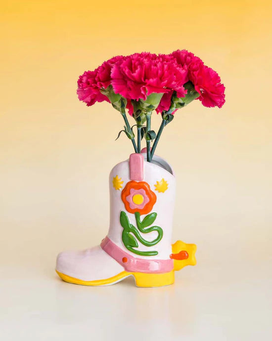 boot shaped vase with orange and yellow flower design and yellow star spur filled with pink carnations.