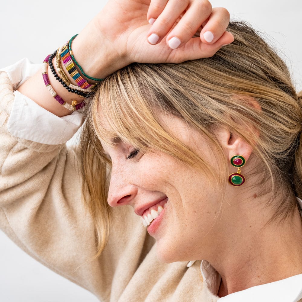 smiling person wearing colorful bracelets and earrings and a beige sweater