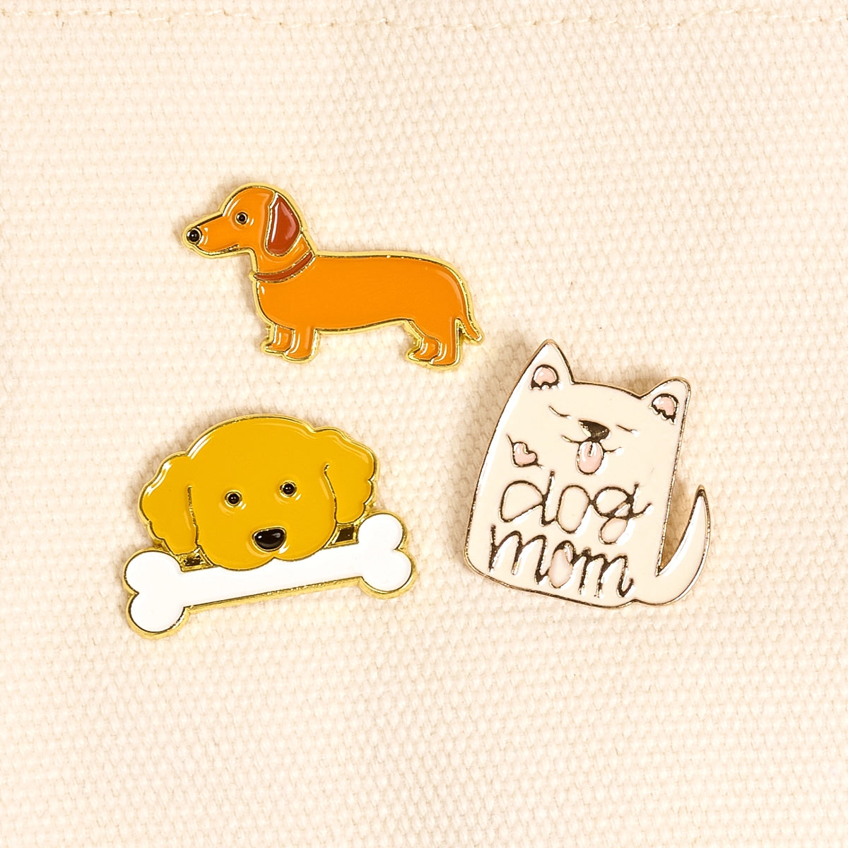 Three dog-themed pins on a beige background