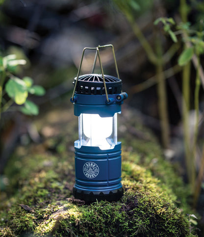 the blue Firefly 2-In-1 Rechargeable Lantern and Fan displayed in the wood on a log