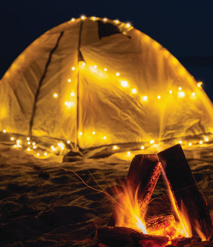 tent lit up with mini lights with a campfire in the foreground.