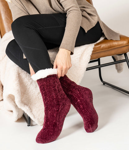 picture of a woman pulling the wine Beyond Soft Slipper Socks while sitting in a chair with a cream colored blanket