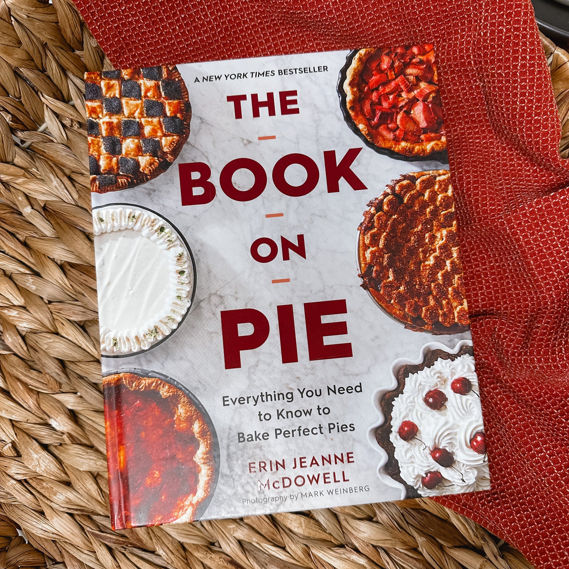 cover of The Book on Pie cookbook, everything you need to know to bake perfect pies by erin jeanne mcdowell in a basket with a red colored kitchen towel.