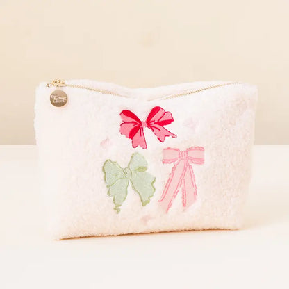 rectangle white fuzzy pouch with three pink and green bows embroidered on it.