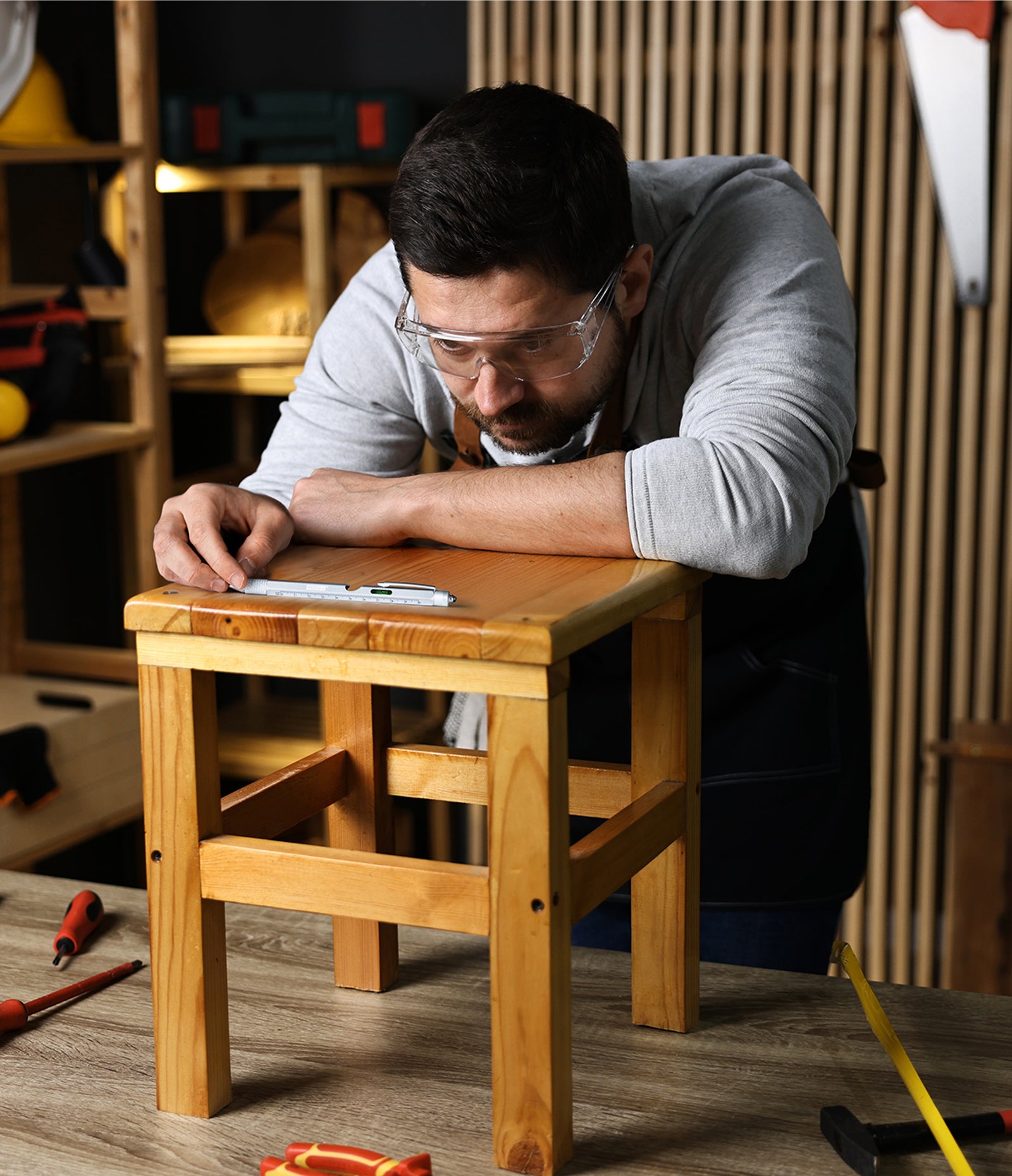 person in a wood-working shop using Level Up 9-In-1 Project Pen to check that a wooden stool is level