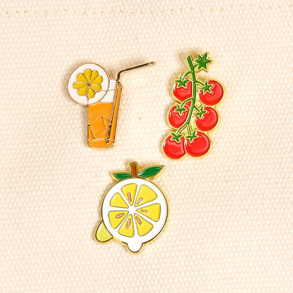 Three colorful fruit-themed pins on a beige fabric background