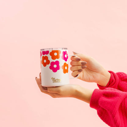 hands holding lovebug floral mug on a pink background.