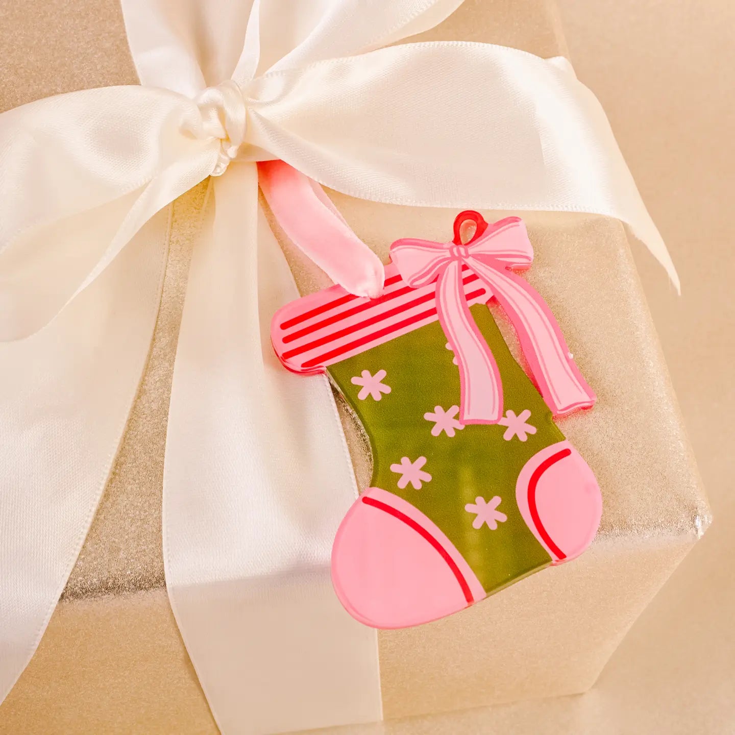 green acyclic stocking ornament with pink trim and a bow tied on a present wrapped in gold