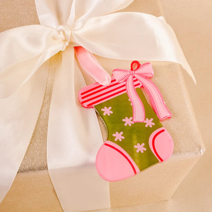 green acyclic stocking ornament with pink trim and a bow tied on a present wrapped in gold