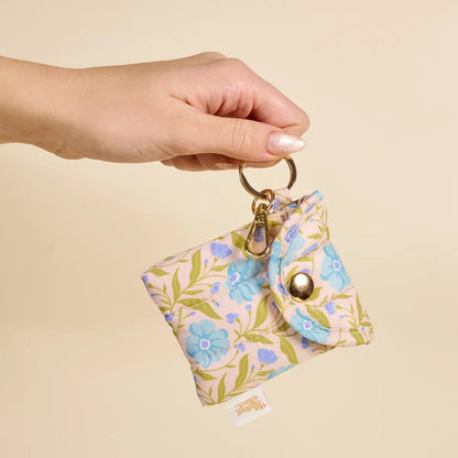 Hand holding a floral keychain pouch against a beige background