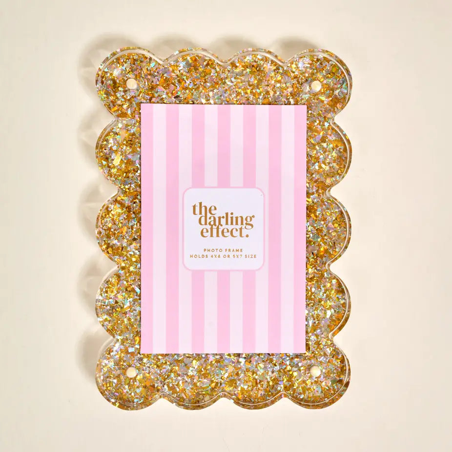 A scalloped photo frame filled with gold glitter, shown with a pink striped insert card that reads 'the darling effect photo frame'.