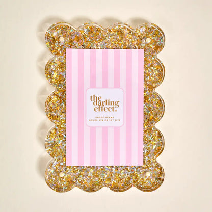 A scalloped photo frame filled with gold glitter, shown with a pink striped insert card that reads 'the darling effect photo frame'.