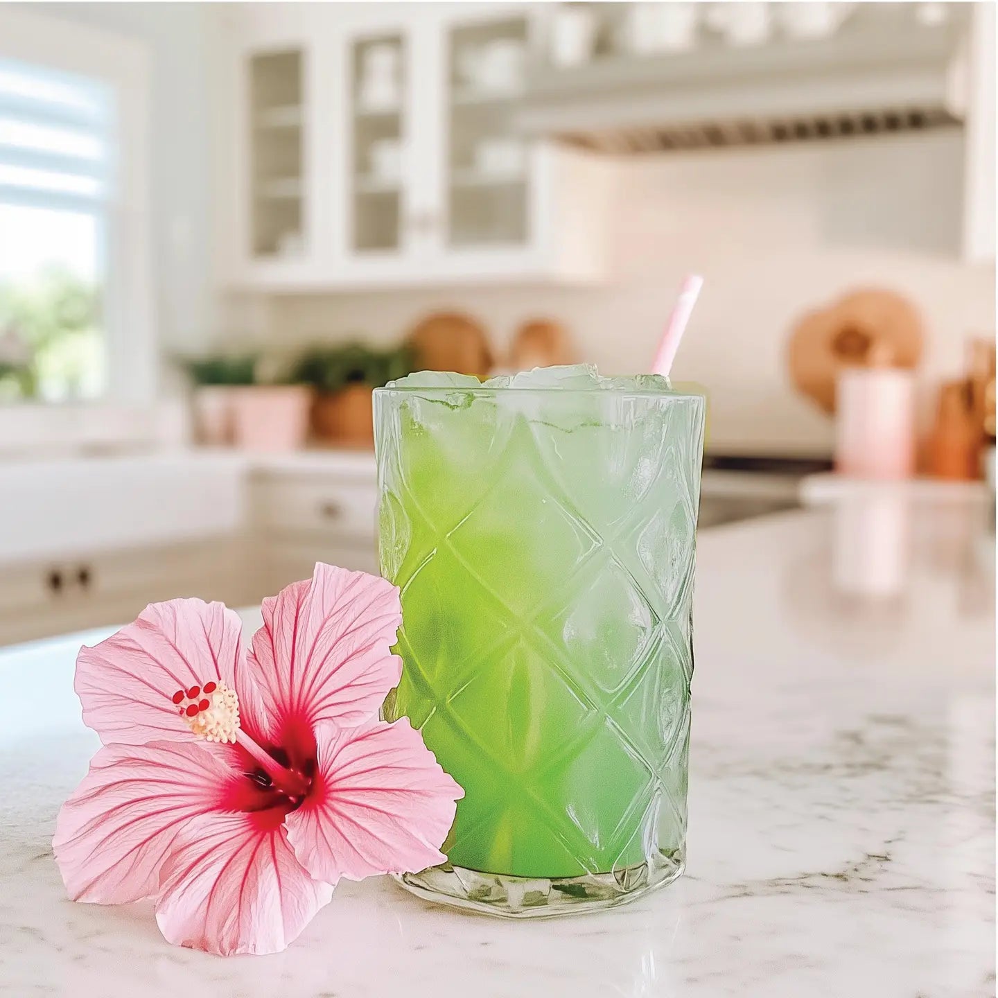 green beverage in a glass on a kitchen counter with a pink hibiscus flower next to it