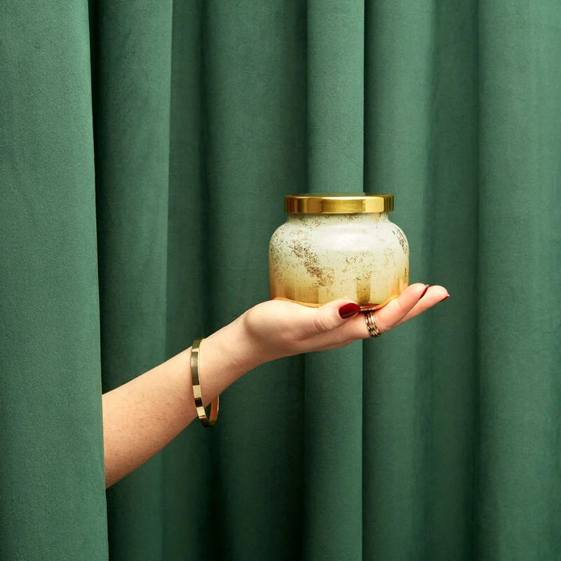 hand holding volcano glimmer jar candle in front of a green curtain.