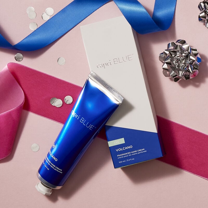 tube of Volcano Hand Cream set next to its box packaging and arranged with silver bows, confetti, and pink and blue ribbons.