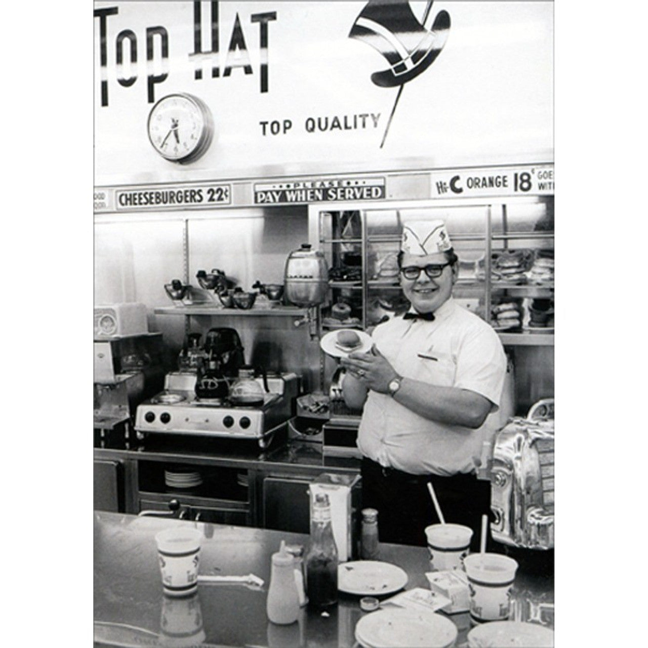 front of card is a man holding a hamburger on a plate inside of a diner in black and white