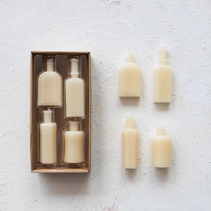 boxed set and unboxed set of bottle shaped candles arranged on a plaster background.