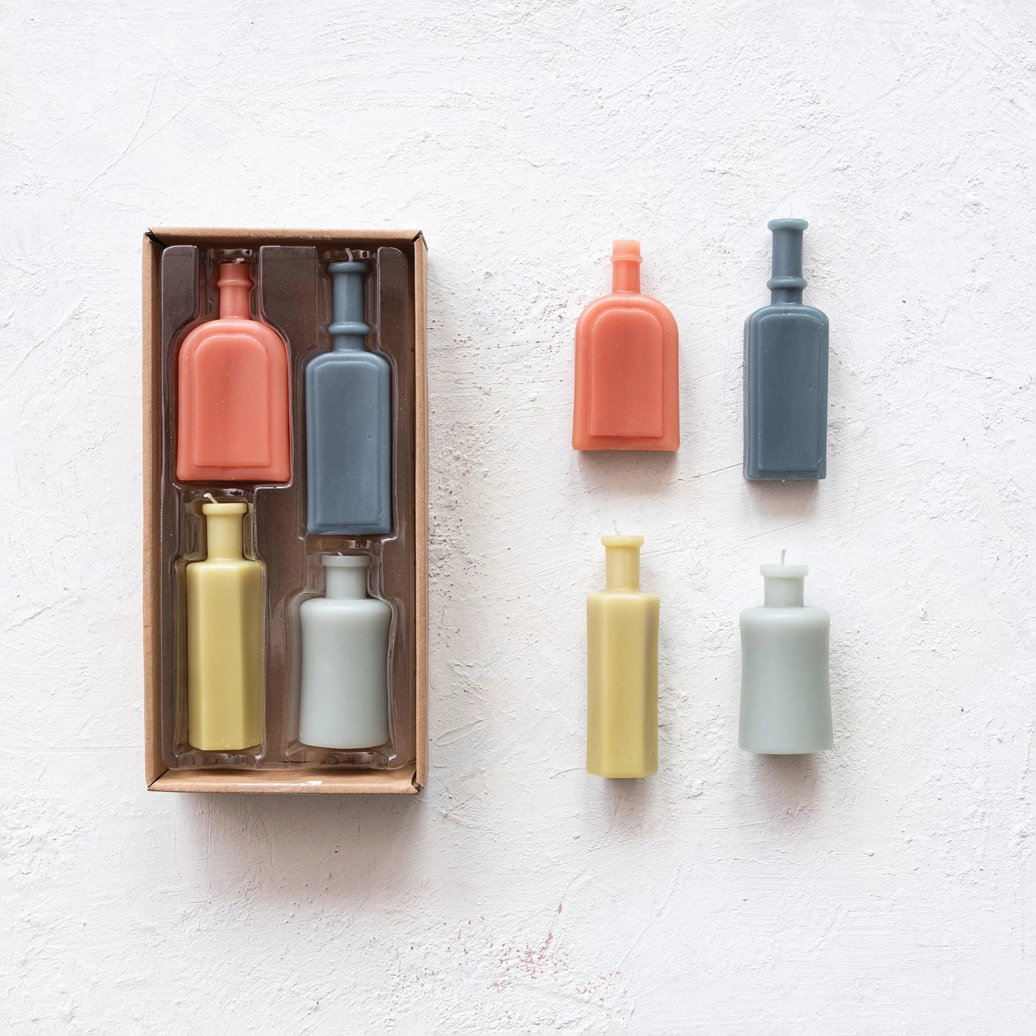boxed set and unboxed set of vintage bottle shaped candles on a plaster background.