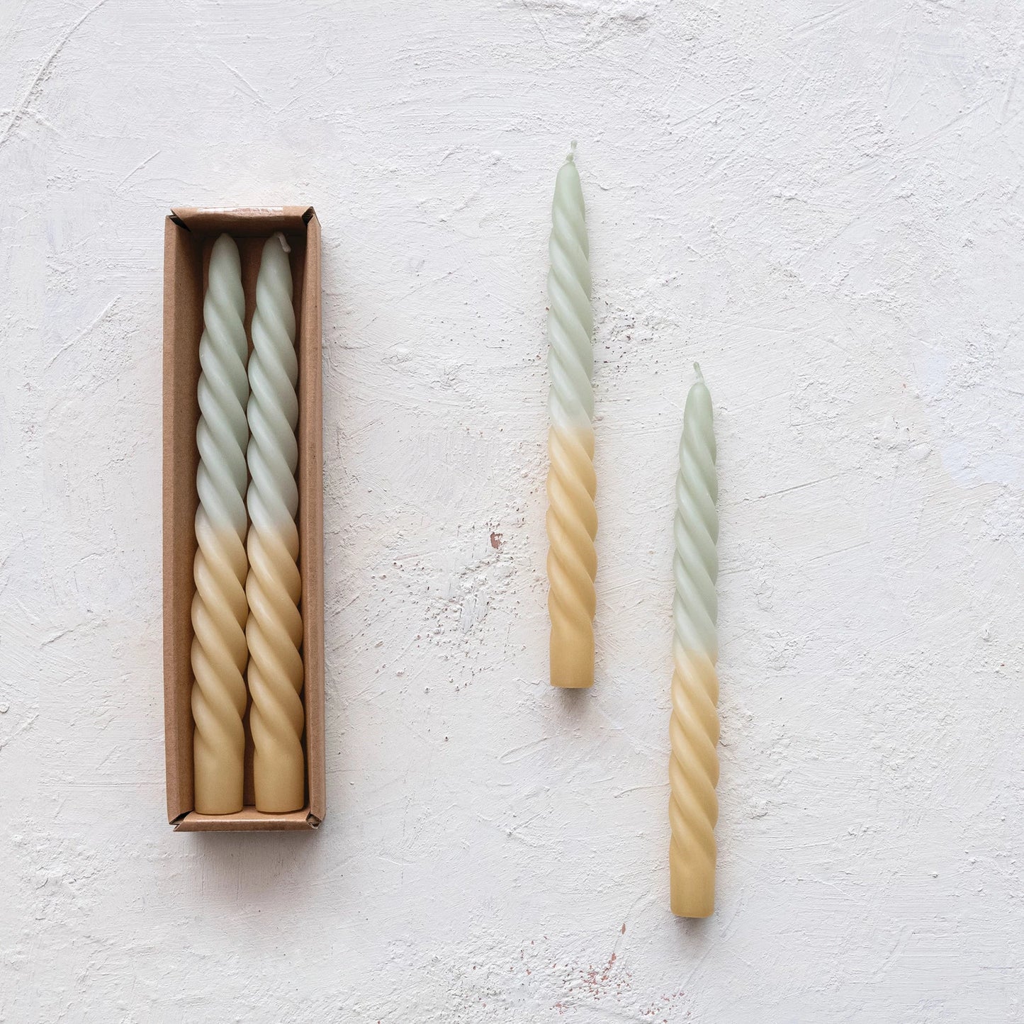 set of mint ombre twisted taper candle set next to a boxed set of candles on a plaster background.