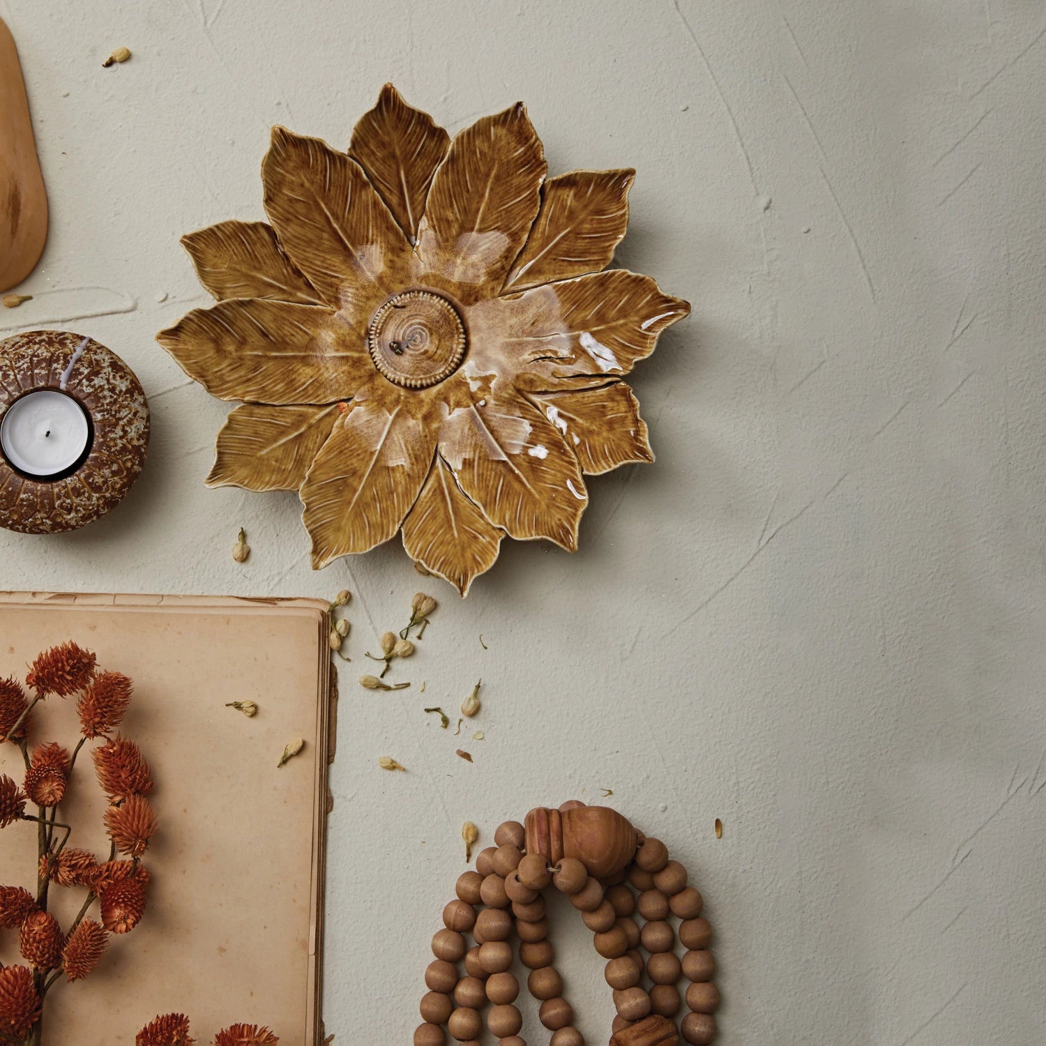 top view of the stoneware flower plate displayed next to a candle, wood bead garland, and dried flowers 