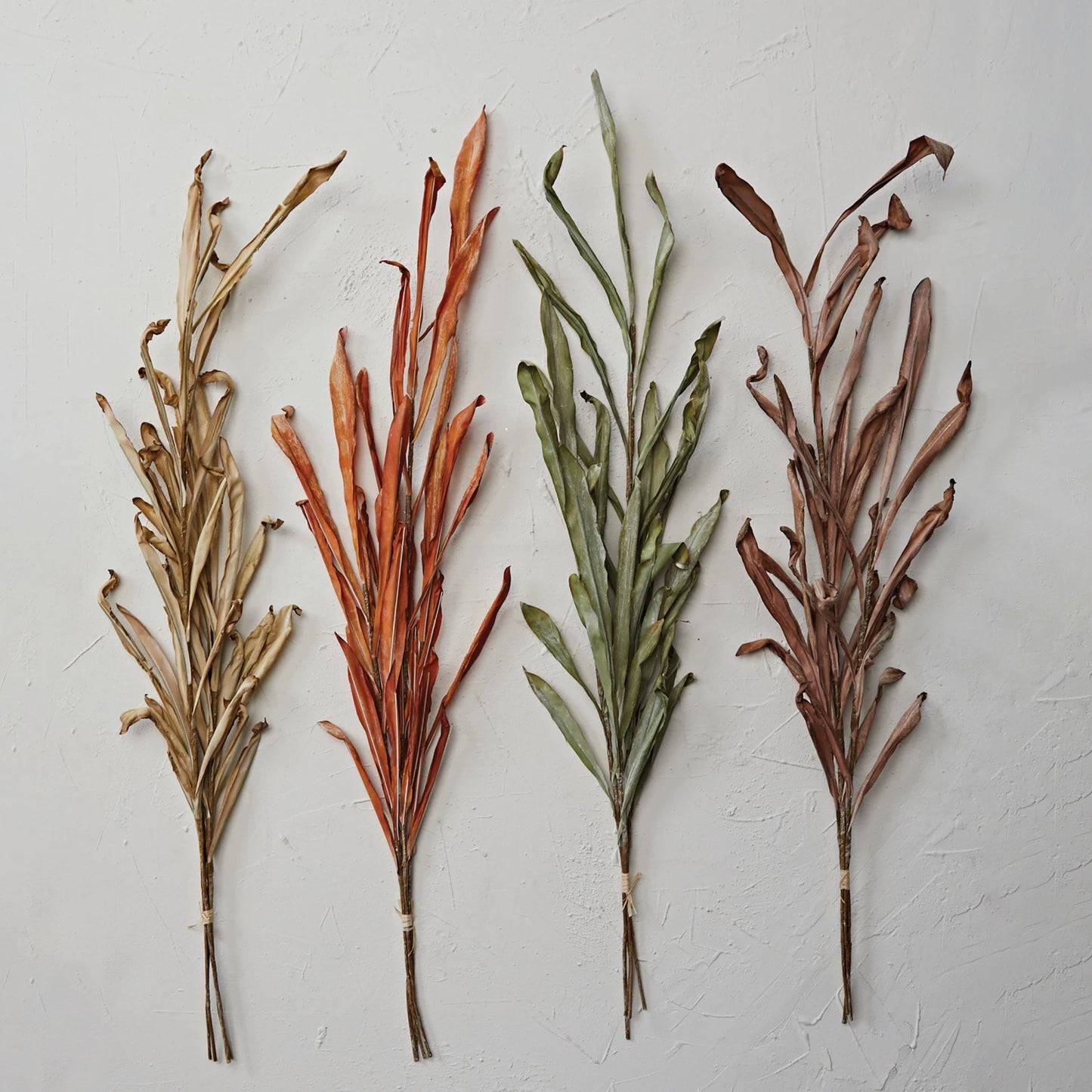 4 colors of fall leaf stems arranged on a plaster background.